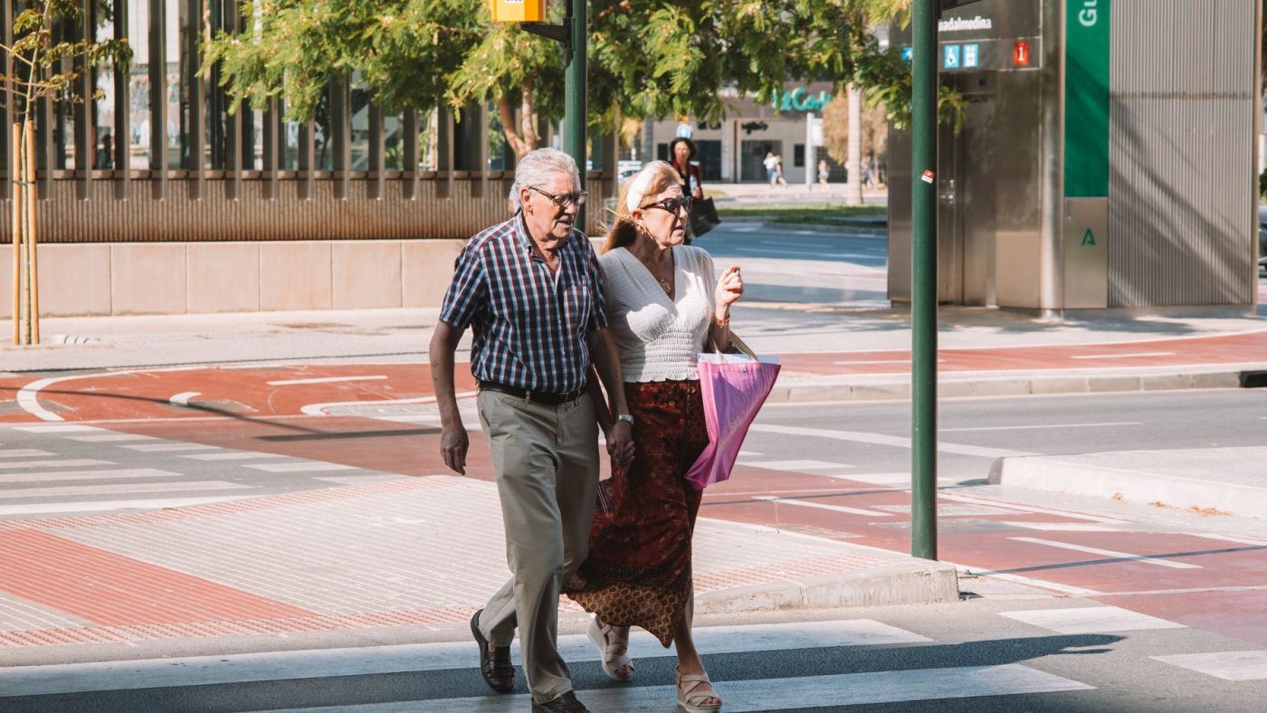 An elderly couple walking across an urban street in sunny Málaga, showcasing city life and companionship.