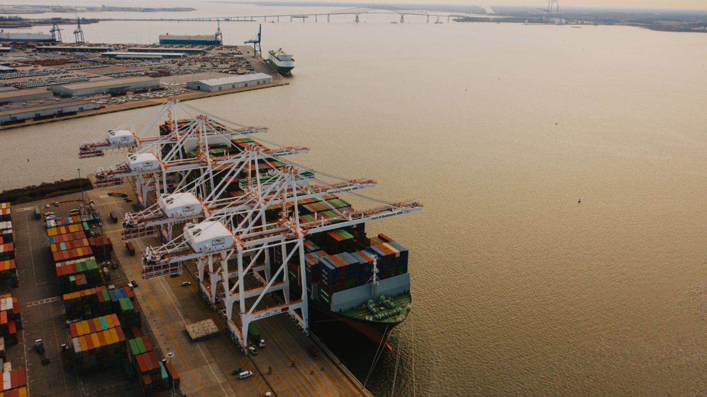 Drone view of cargo containers loaded on long ship on river of pier with lifting cranes