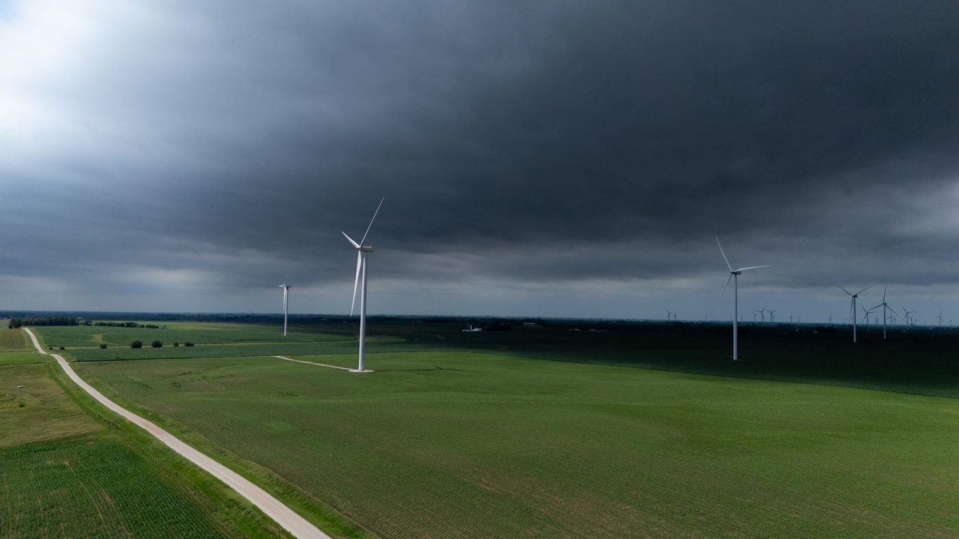 A stormy sky looms over a vast green landscape with wind turbines generating renewable energy.